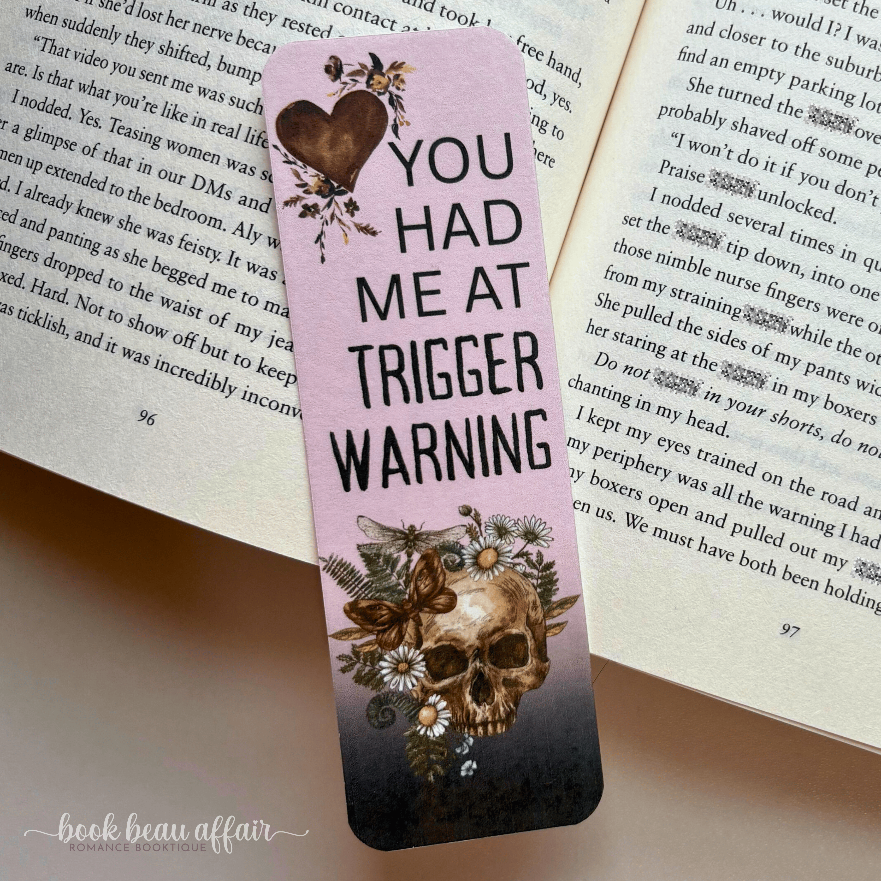 Bookmark with skull design and text 'YOU HAD ME AT TRIGGER WARNING' on an open book.