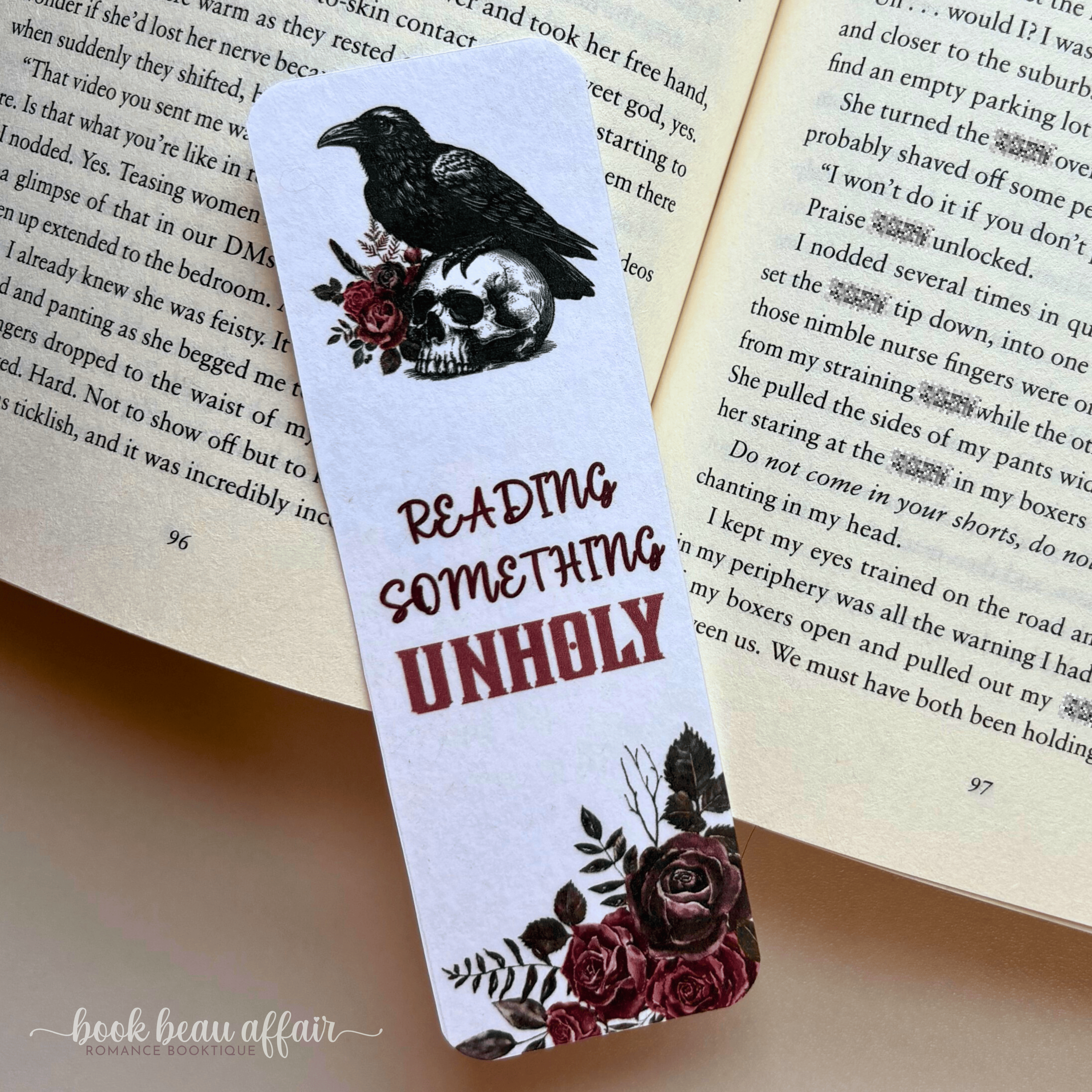 Bookmark with a raven and skull design on an open book that says reading something unholy