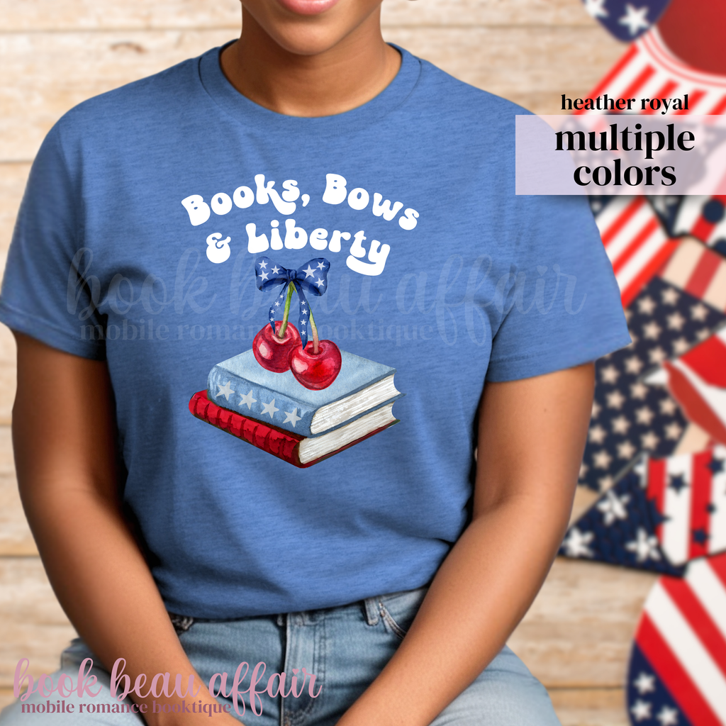 Person wearing a blue t-shirt with 'Books, Bows & Liberty' design in front of American flags.