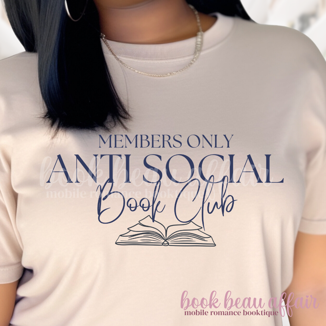 Close up of A woman wearing a light sand colored graphic t-shirt with navy blue text that reads 'MEMBERS ONLY ANTI SOCIAL Book Club' and an illustration of an open book. 