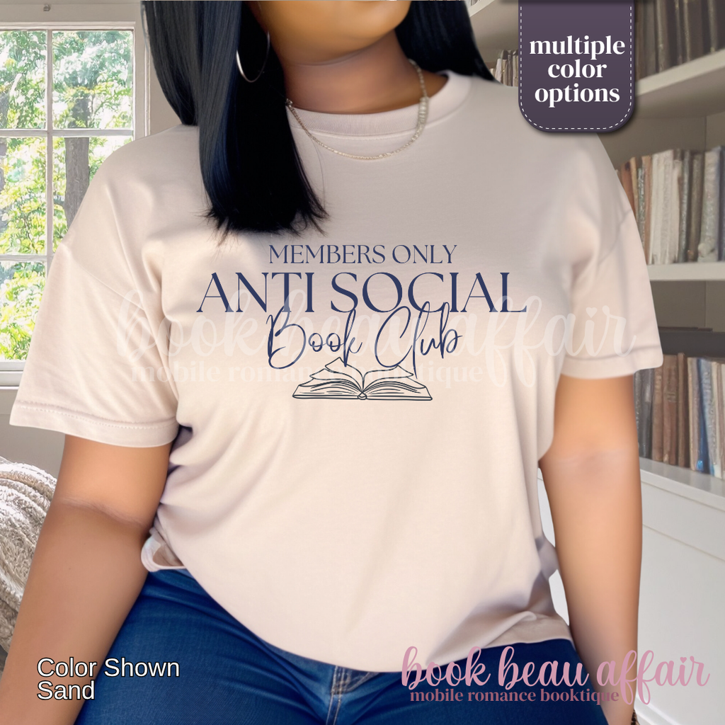 A woman wearing a light sand-colored graphic t-shirt with navy blue text that reads 'MEMBERS ONLY ANTI SOCIAL Book Club' and an illustration of an open book. 
