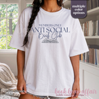 A woman wearing a white graphic t-shirt with navy blue text that reads 'MEMBERS ONLY ANTI SOCIAL Book Club' and an illustration of an open book. 