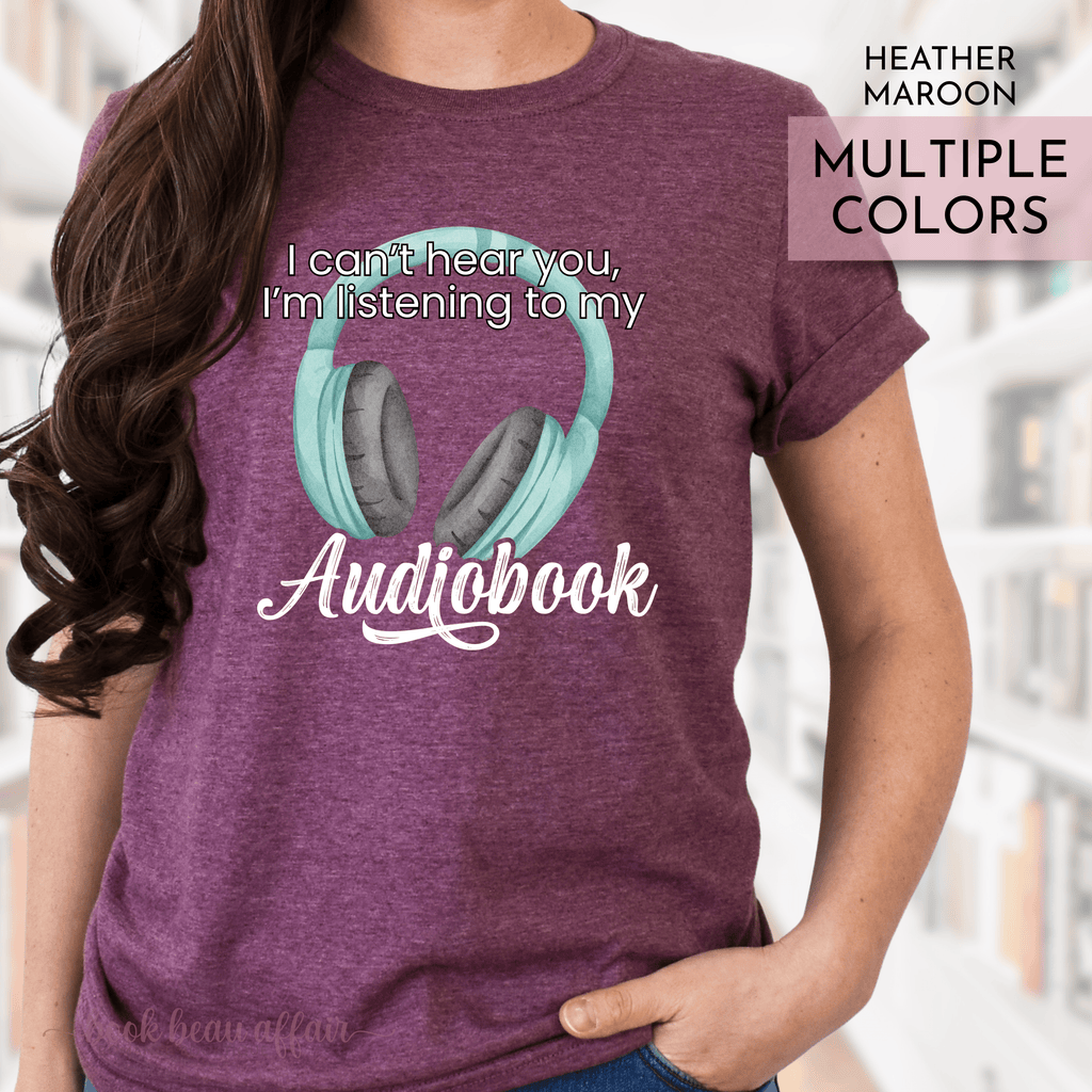 Maroon t-shirt with headphones graphic and text 'I can't hear you, I'm listening to my Audiobook' on a blurred background.