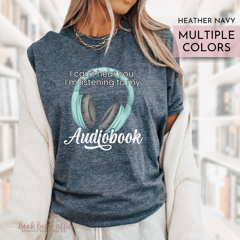 Heather navy tshirt with headphones graphic and text 'I can't hear you, I'm listening to my audiobook' worn by a person.