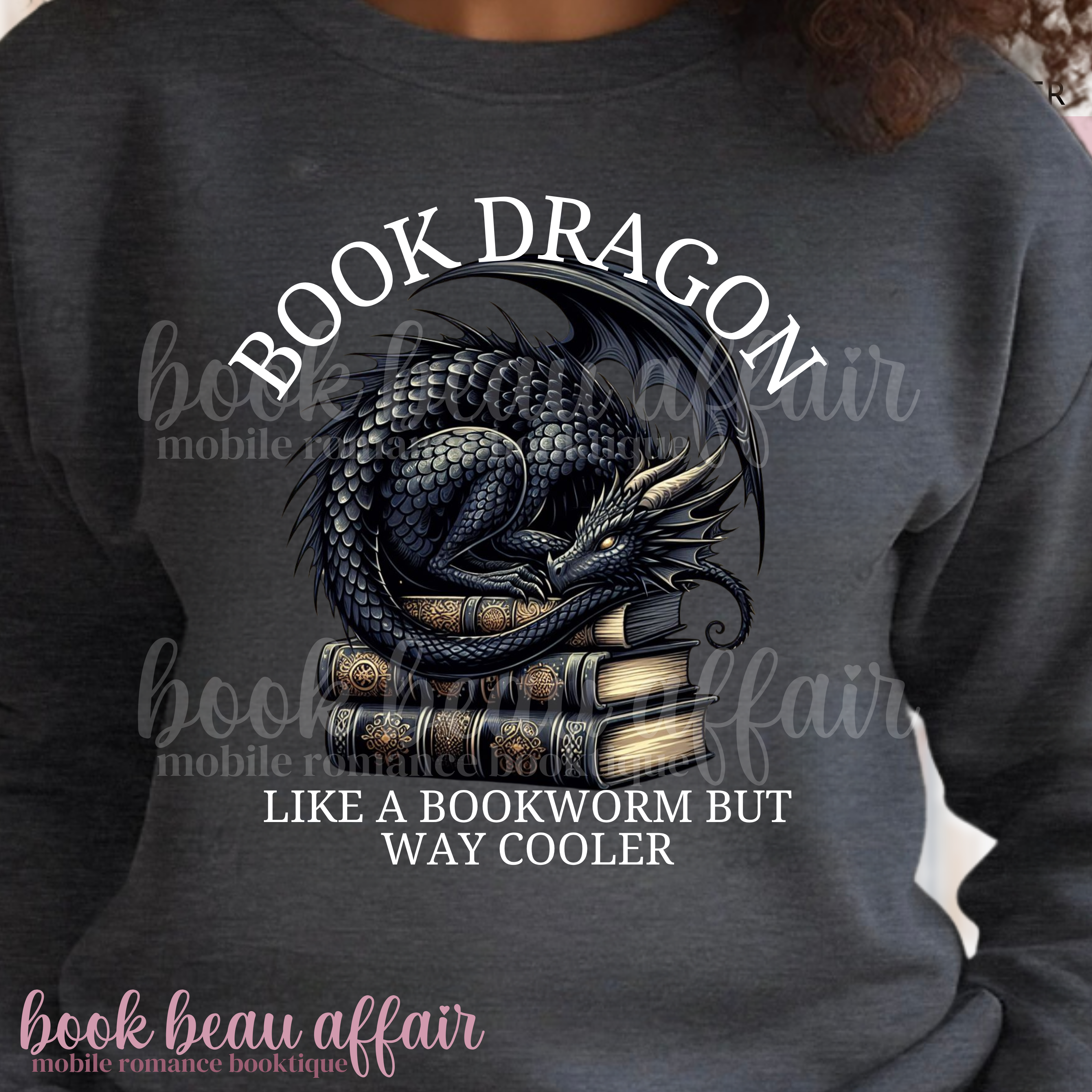 Gray sweatshirt with a dragon laying on a stack of books and text that says book dragon, like a bookworm but way cooler