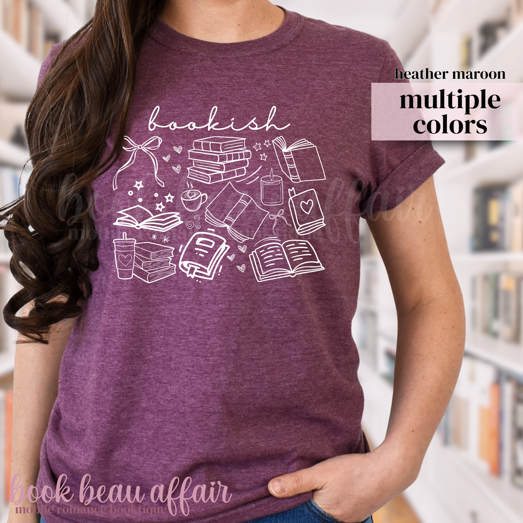 Person wearing a maroon t-shirt with book-themed graphics in a library setting