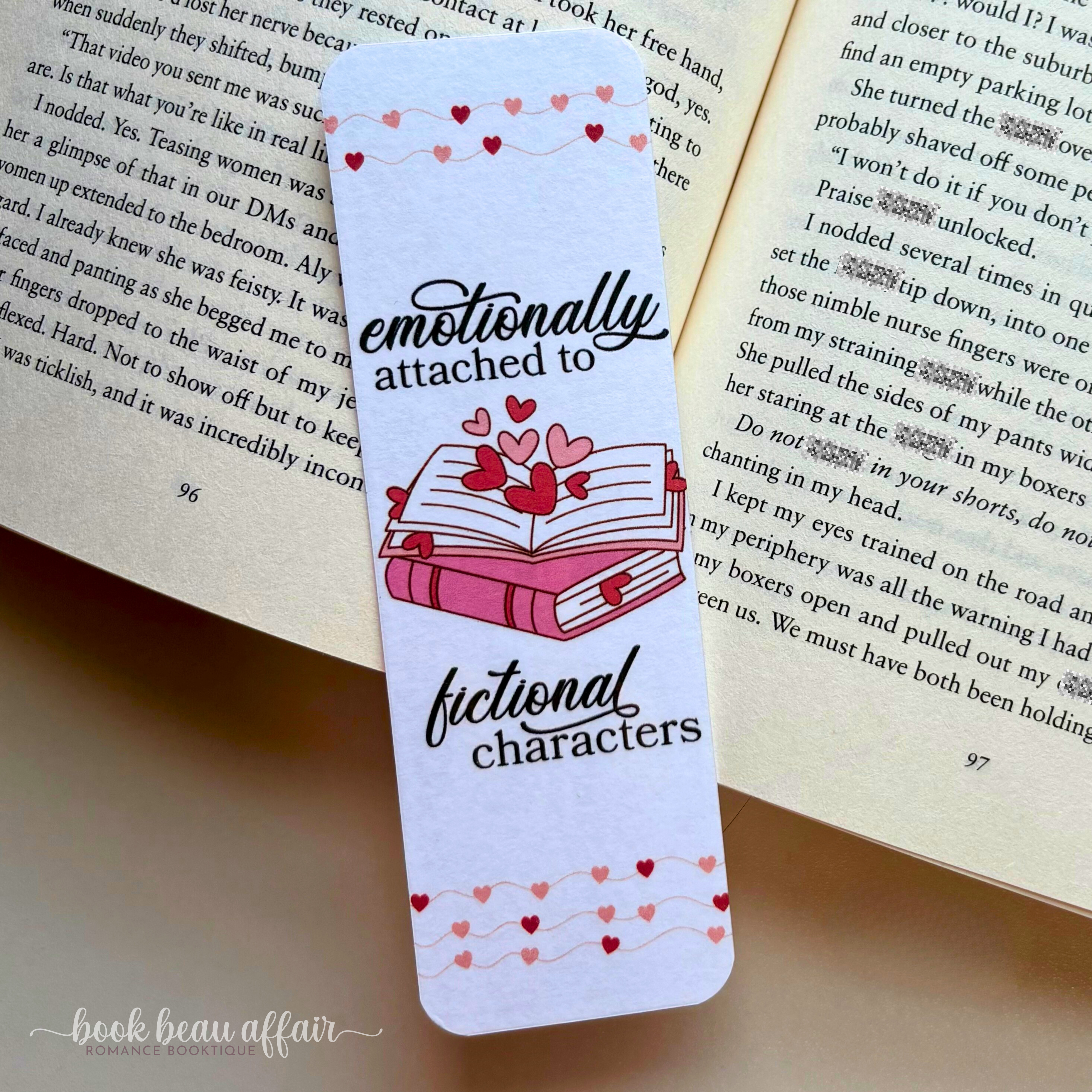 Bookmark with hearts and text 'emotionally attached to fictional characters' on an open book.