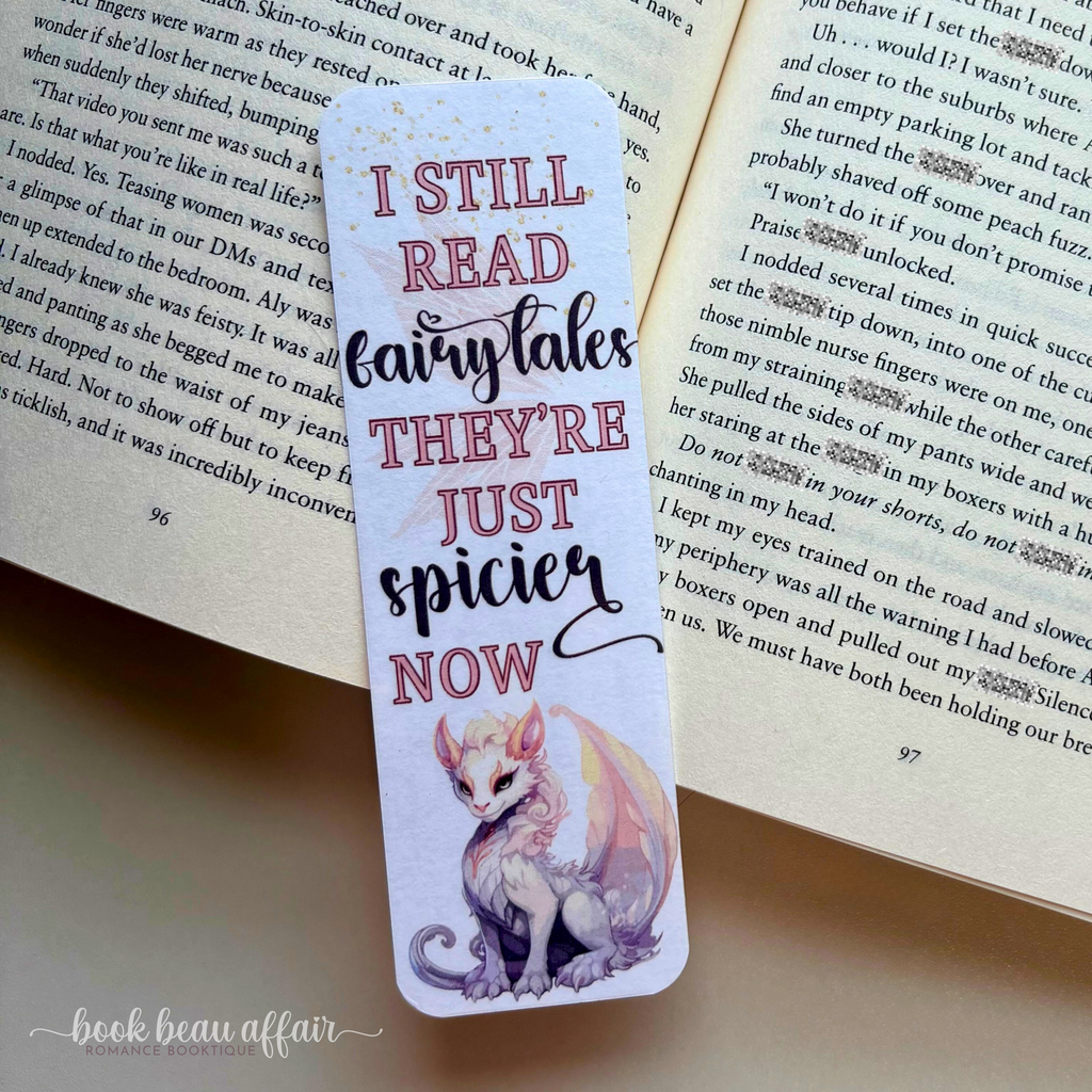 Bookmark with dragon illustration and text on an open book. The text says I still read fairytales they're just spicier now