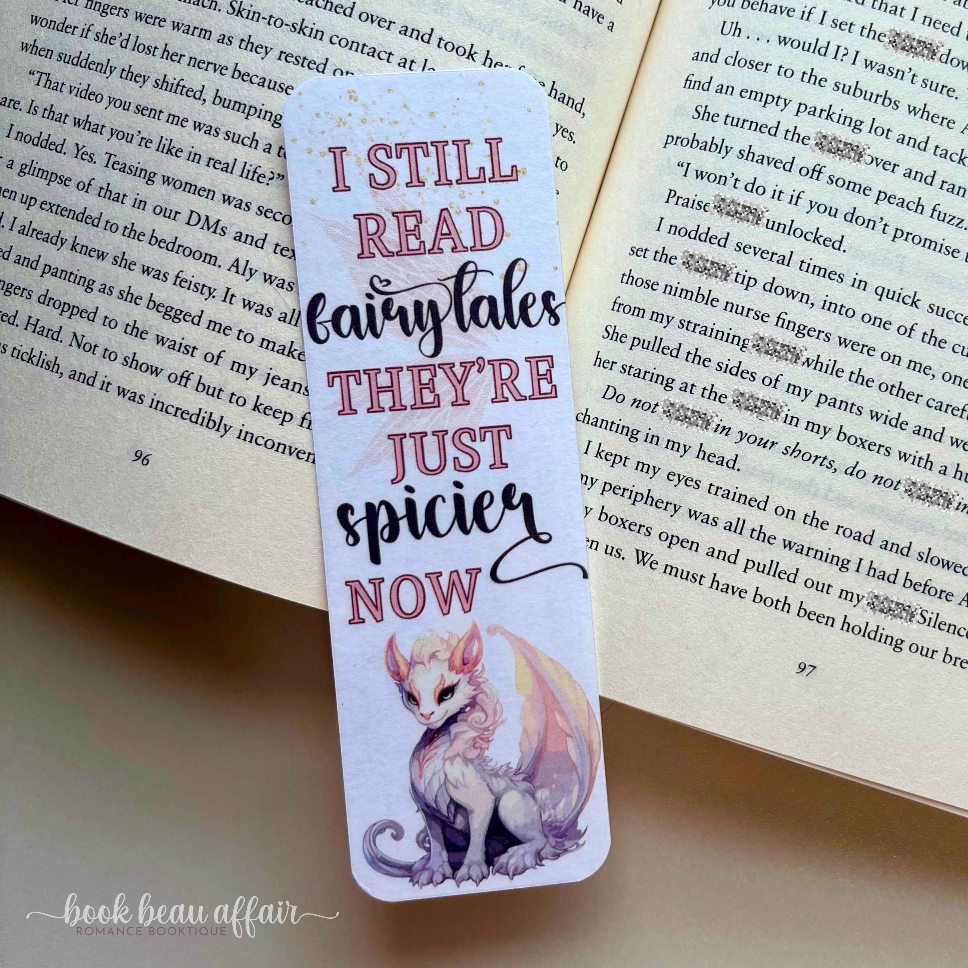 Bookmark with dragon illustration and text on an open book. The text says I still read fairytales they're just spicier now