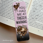 Bookmark with skull design and text 'YOU HAD ME AT TRIGGER WARNING' on an open book.