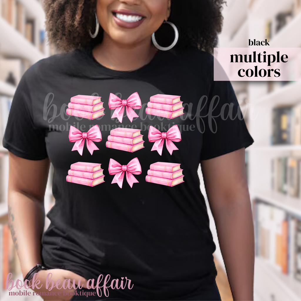 person wearing a black t-shirt with pink bows and pink stacks of books.