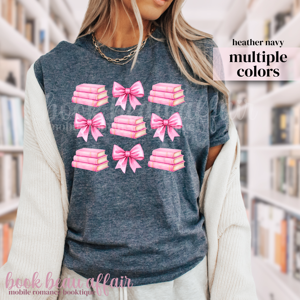 person wearing a heather navy t-shirt with pink bows and pink stacks of books.