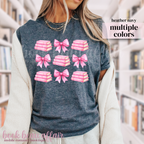 person wearing a heather navy t-shirt with pink bows and pink stacks of books.