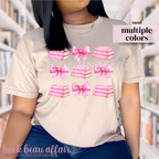 person wearing a beige t-shirt with pink bows and pink stacks of books.