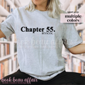 Person wearing a gray t-shirt with 'Chapter 55. #IYKYK' text, sitting outdoors.