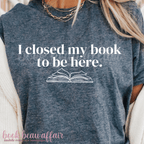 Blue t-shirt with 'I closed my book to be here' text and book graphic, worn by a person.