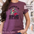 Person wearing a maroon t-shirt with a snake and rose design and text 'Protected by the Vipers' in a library setting.