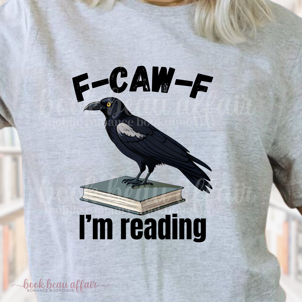 Gray t-shirt with a crow on a book graphic and text 'F-CAW-F I'm reading' on a blurred background.