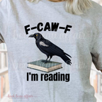 Gray t-shirt with a crow on a book graphic and text 'F-CAW-F I'm reading' on a blurred background.