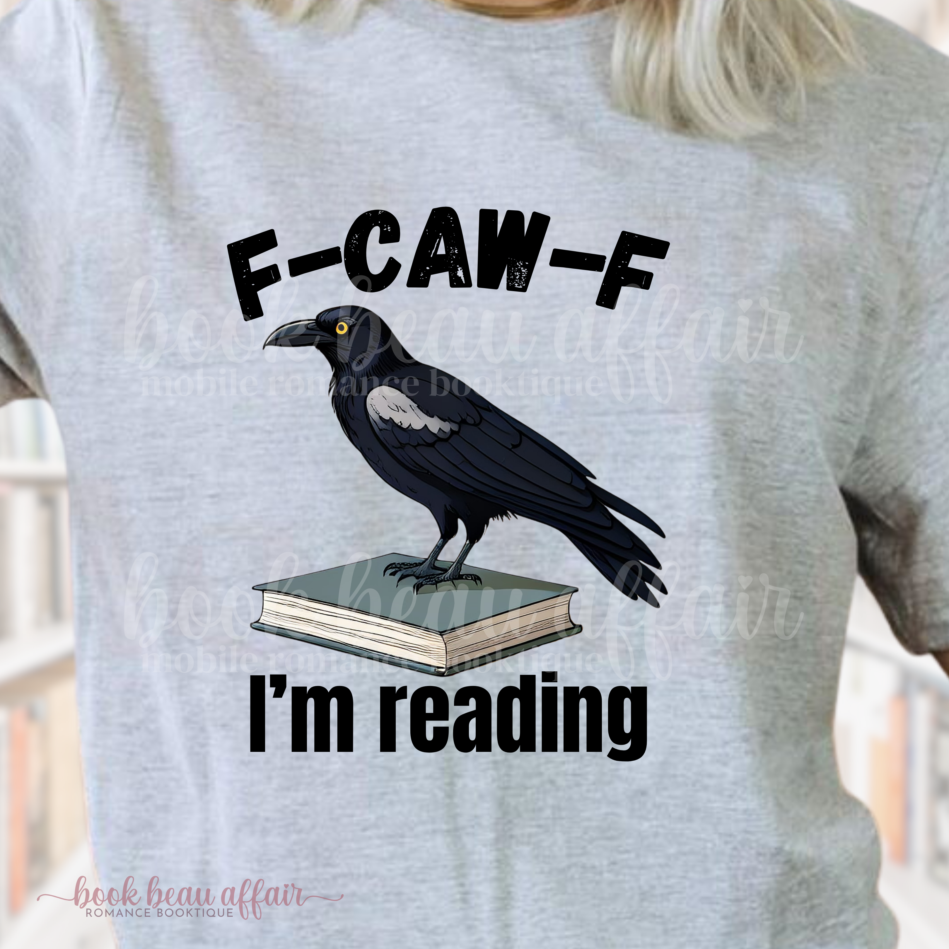Gray t-shirt with a crow on a book graphic and text 'F-CAW-F I'm reading' on a blurred background.