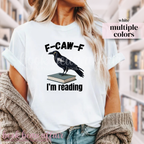 White t-shirt with a crow on a book graphic and text 'F-CAW-F I'm reading' 
