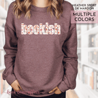 Heather dark maroon sweatshirt with 'bookish' text in multiple colors, worn by a person.