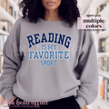 Person wearing a gray sweatshirt with 'Reading is my favorite sport' text in a library setting