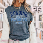 Person wearing a blue t-shirt with 'Reading is my favorite sport' text in a library setting.