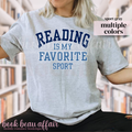 Person wearing a gray t-shirt with 'Reading is my favorite sport' text in a library setting