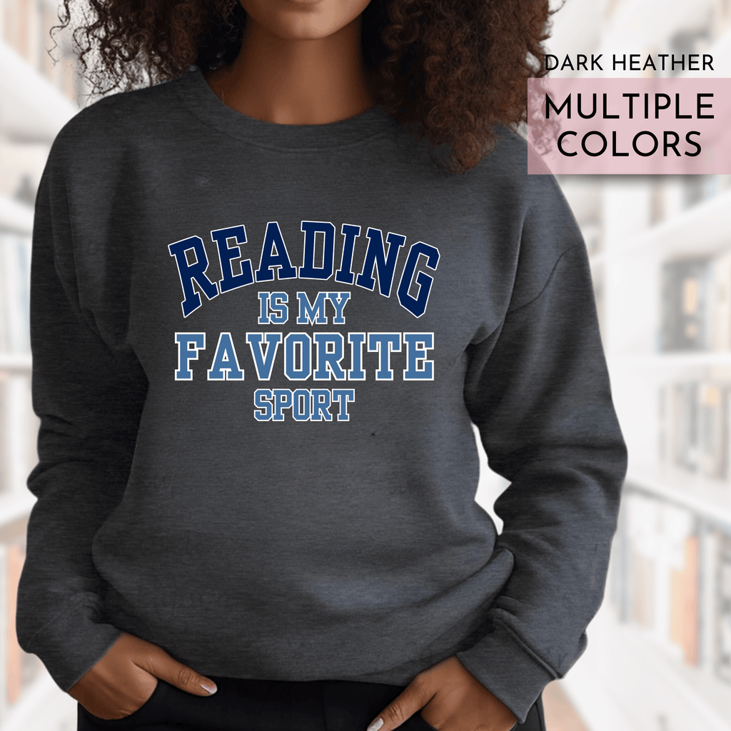 Person wearing a dark heather sweatshirt with 'Reading is my favorite sport' text in a library setting.