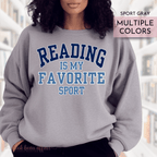 Gray sweatshirt with 'Reading is my favorite sport' text worn by a person, with a blurred background.