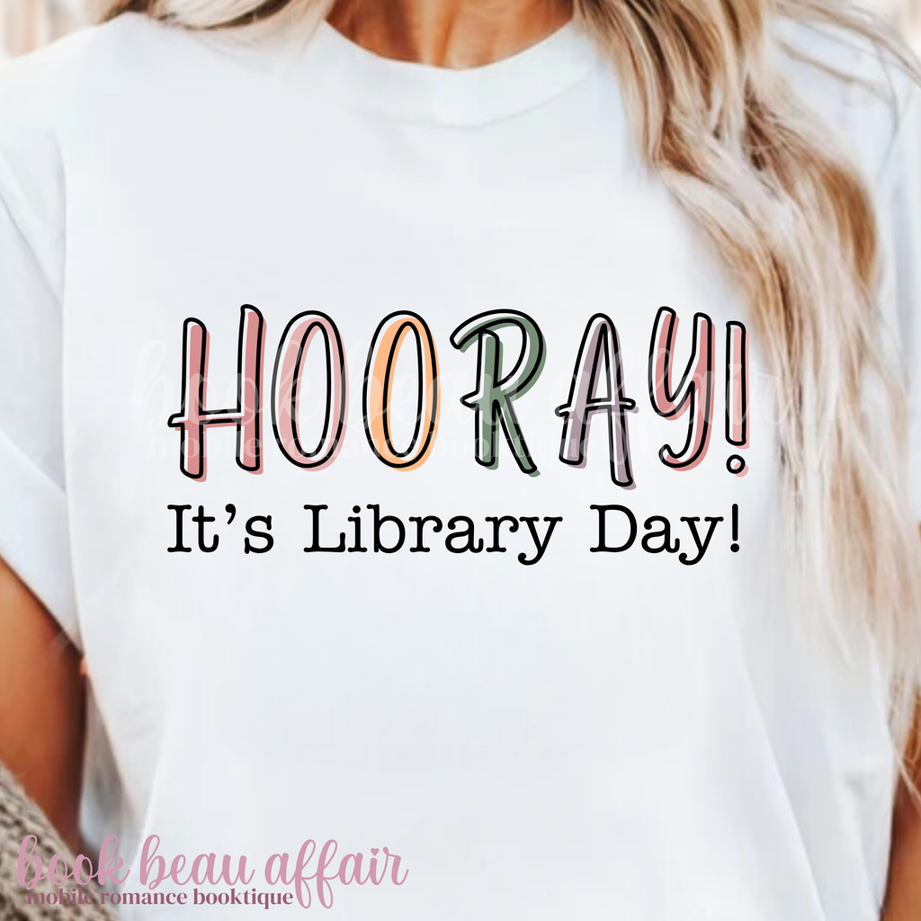White t-shirt with 'HOORAY! It's Library Day!' text worn by a person.