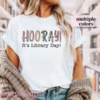 White t-shirt with 'HOORAY! It's Library Day!' text worn by a person.