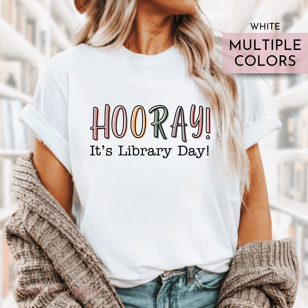 A person wearing a white t-shirt with the text 'HOORAY! It's Library Day!' printed on the front.