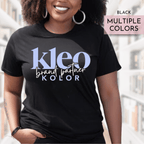 Person wearing a black t-shirt with 'Kleo Kolor Brand Partner' text, standing in an urban setting.