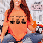 Person wearing an orange t-shirt with skeleton graphics and text read in peace, holding a mug with ghost design.