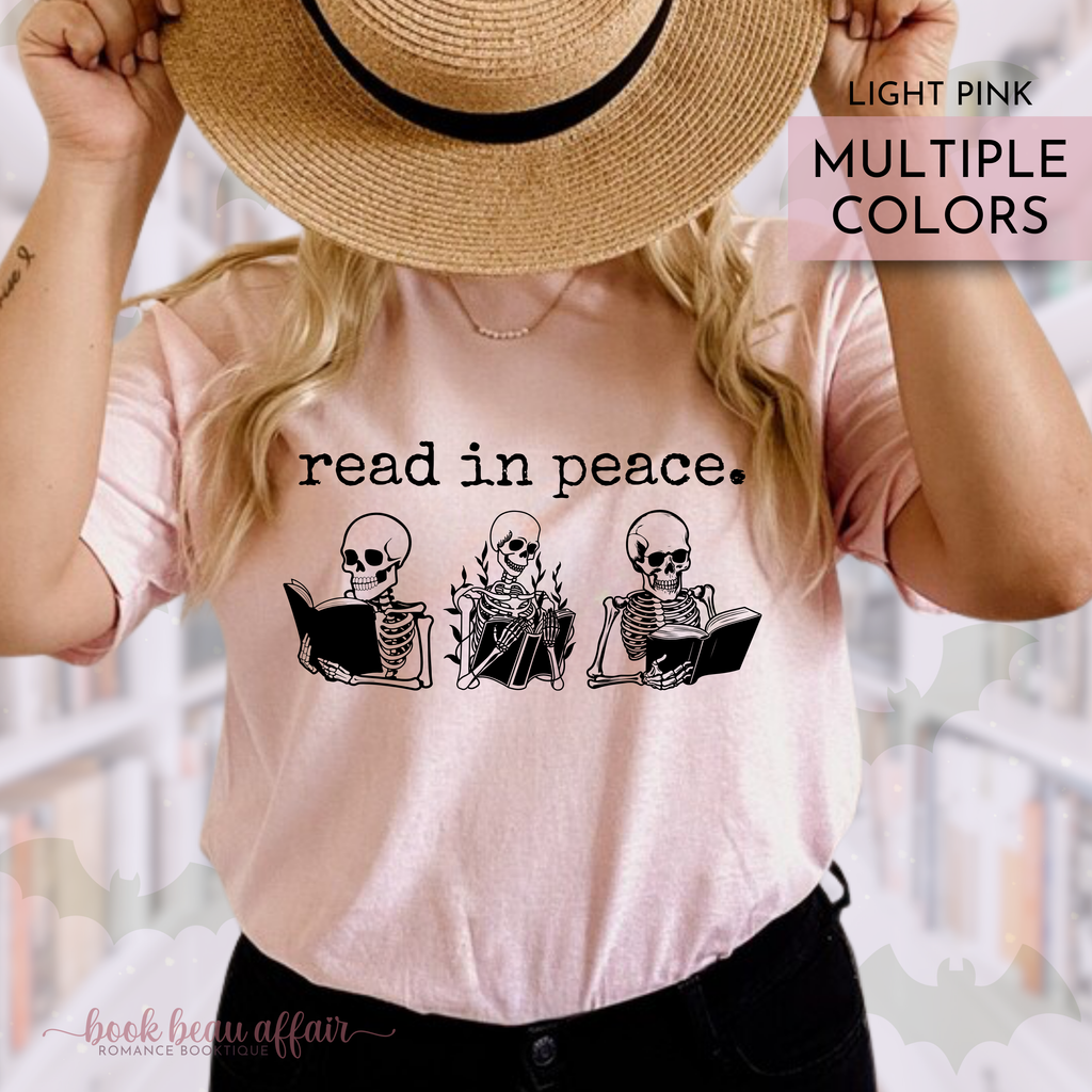 Person wearing a light pink t-shirt with skeleton graphics and text that says read in peace, holding a straw hat.