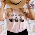 Person wearing a light pink t-shirt with skeleton graphics and text that says read in peace, holding a straw hat.