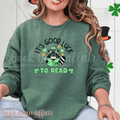 St. Patricks Day Themed Shirt. Illustration of a raccoon holding a green book with text that says "It's Good Luck to Read"