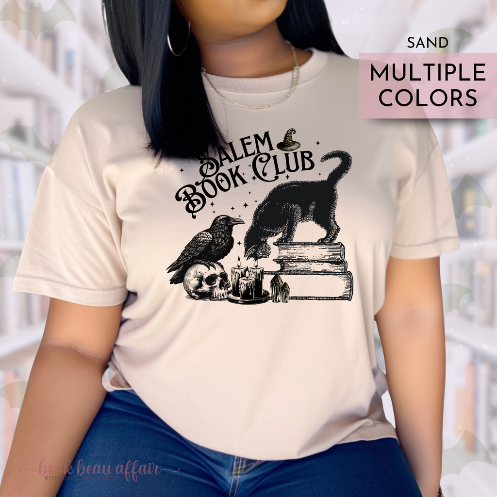 Person wearing a tan shirt that says Salem Book Club in text and has a black cat sitting on books