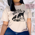 Person wearing a tan shirt that says Salem Book Club in text and has a black cat sitting on books