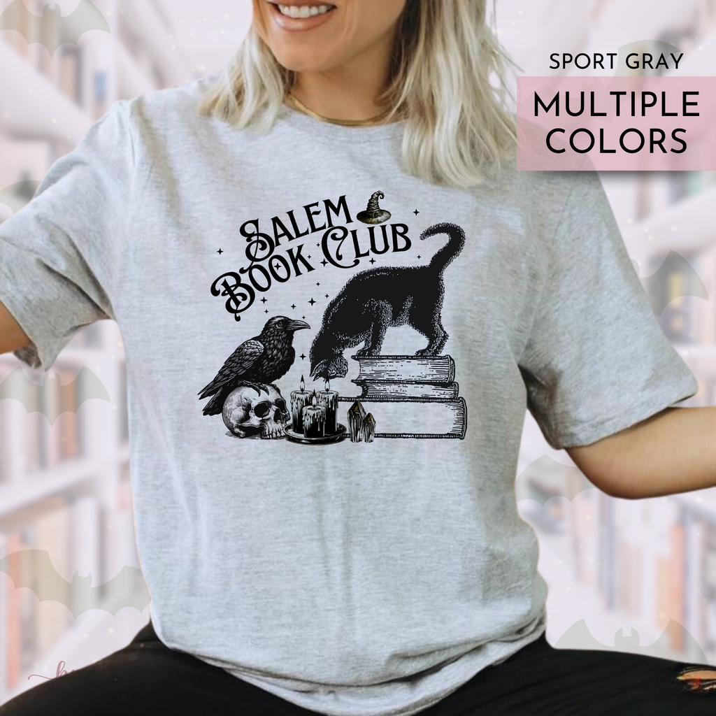 Person wearing a gray t-shirt with 'Salem Book Club' design, featuring a black cat, bird, and skull.