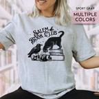 Person wearing a gray t-shirt with 'Salem Book Club' design, featuring a black cat, bird, and skull.