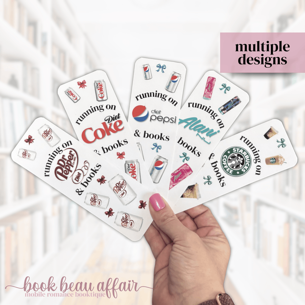 Hand holding multiple bookmarks with various diet soda brand logos and text, with a blurred indoor background.