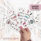 Hand holding multiple bookmarks with various diet soda brand logos and text, with a blurred indoor background.