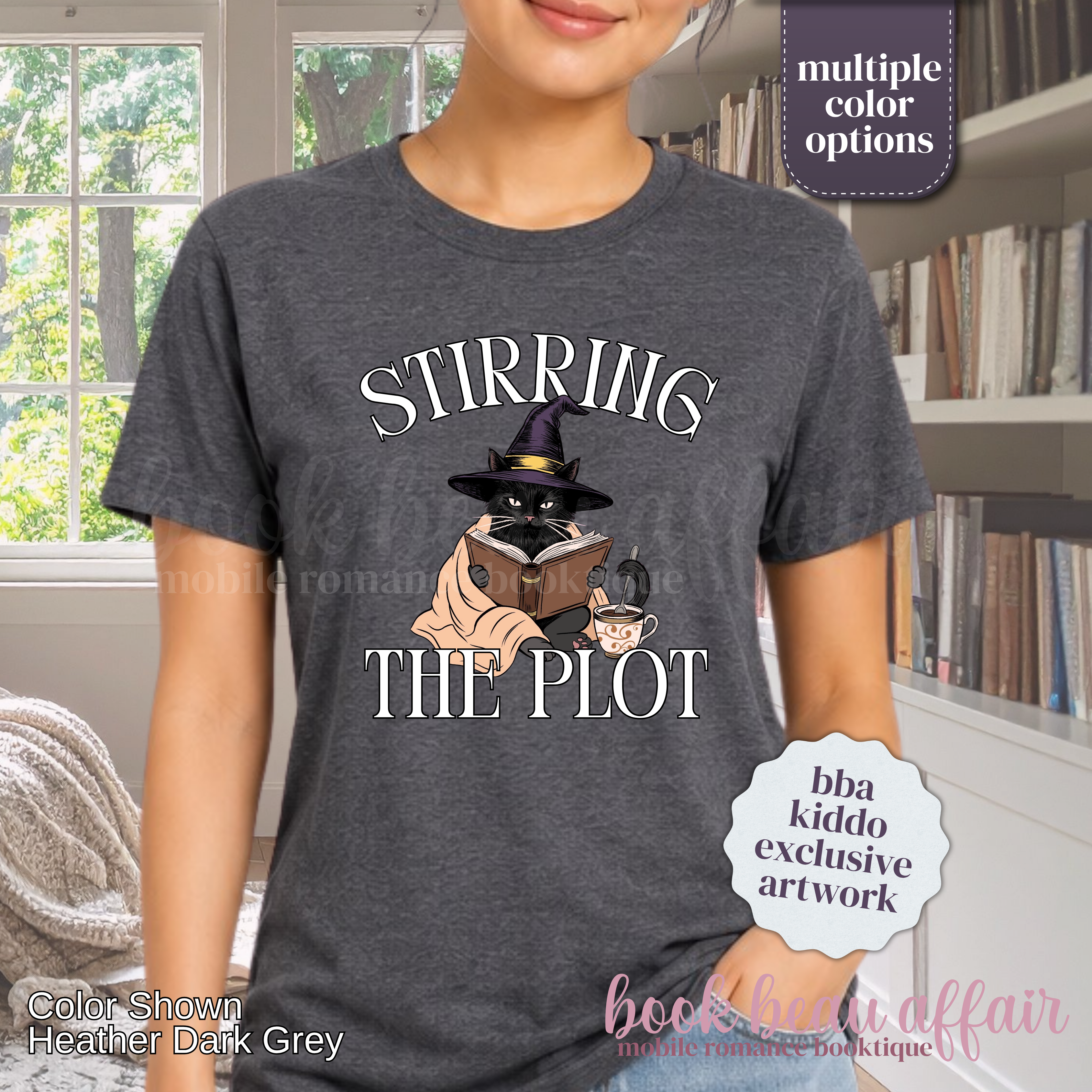A woman wearing a dark gray graphic t-shirt with the text 'STIRRING THE PLOT' and an illustration of a cat in a witch hat reading a book. 